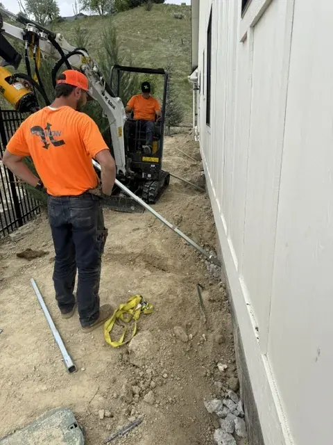 Crew installing a helical tieback anchor outside a home